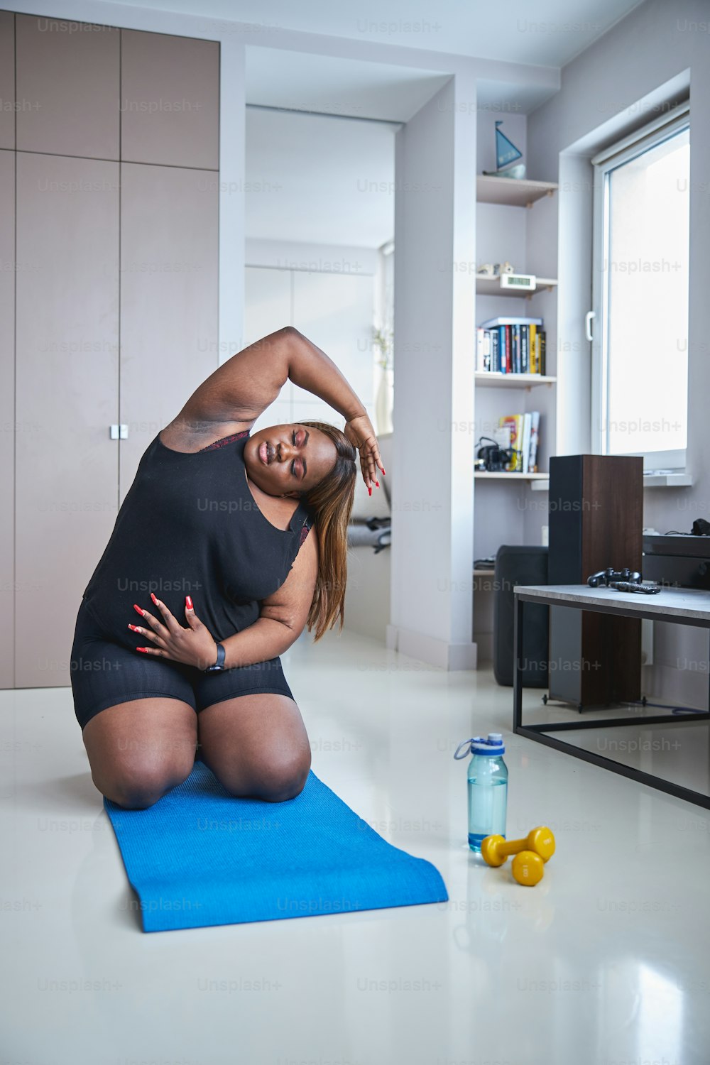Lovely African American woman stretching while sitting on fitness mat on her home floor