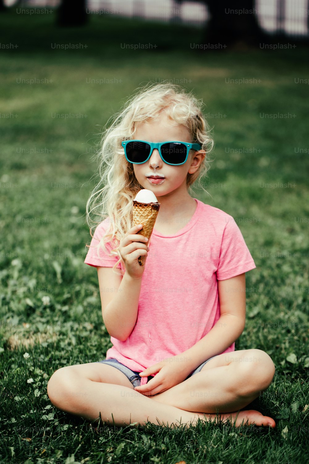 더러운 코와 콧수염을 가진 선글라스를 쓴 귀여운 재미있는 사랑스러운 소녀가 와플 콘에서 아이스크림을 먹고 있습니다. 야외에서 맛있는 달콤한 추운 여름 제철 음식을 먹는 행복하고 시원한 힙스터 아이. 여름의 즐거움.