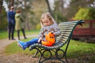 Adorable little girl sitting on the bench with lunchbox and having picnic on a spring day. Child enjoying healthy snack in park. Outdoor spring activity for small kids