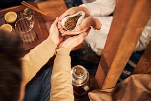 Primer plano de un hombre joven que toma las manos de la mujer con hojas de té secas mientras está sentado en la mesa en la casa de t�é