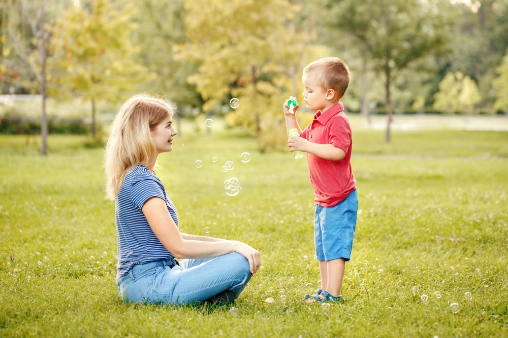 젊은 백인 어머니와 소년 유아 아들은 공원에서 비누 방울을 불고 있습니다. 엄마와 아이는 여름날 야외에서 함께 놀고 있습니다. 행복 한 정통 가족 어린 시절 생활 방식.
