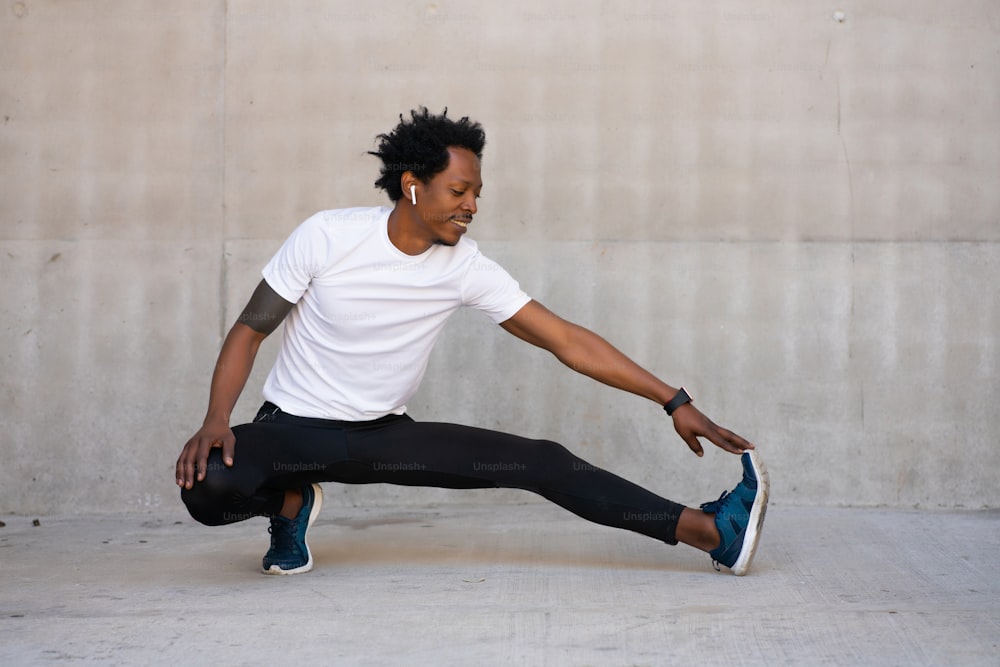 Uomo atletico afro che allunga le gambe e si riscalda prima dell'esercizio all'aperto. Concetto di sport e stile di vita sano.