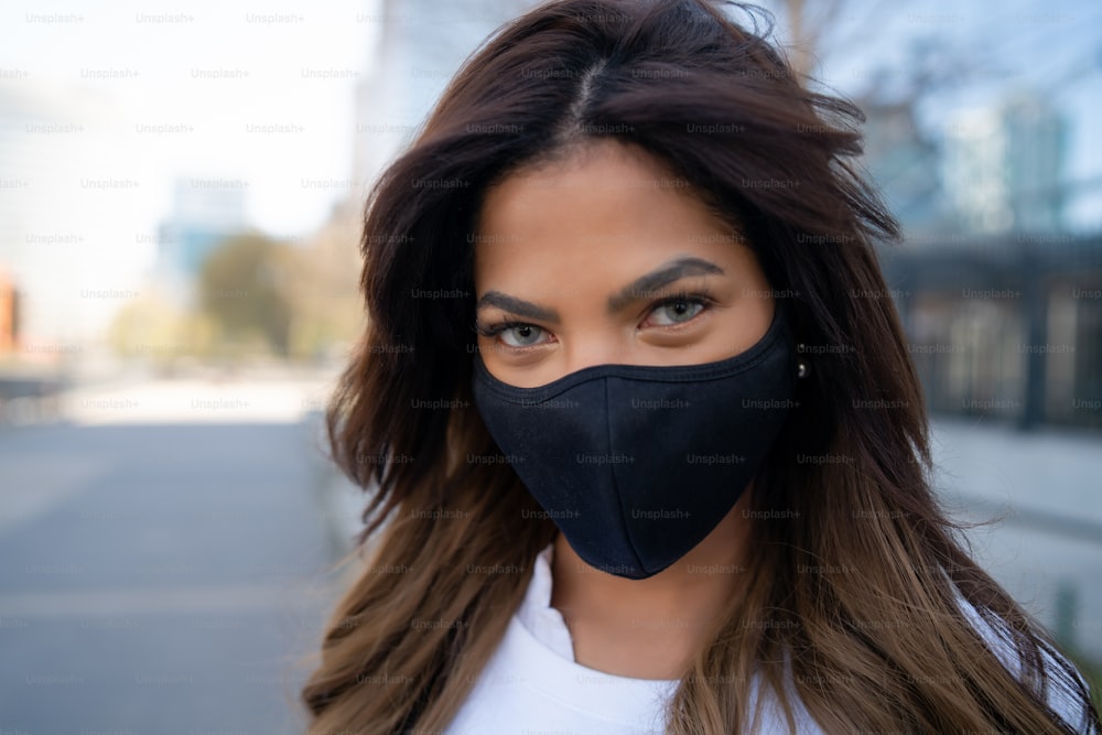 屋外の路上に立っているときにフェイスマスクを着用している若い女性の接写。アーバンコンセプト。ニューノーマルなライフスタイルのコンセプト。