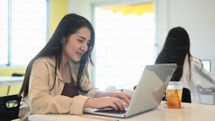 クリエイティブなオフィスで同僚と座りながら、コンピューターのラップトップで作業している笑顔の若い女性デザイナー。