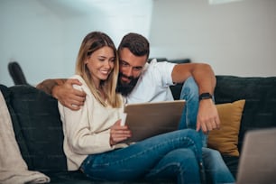 Shot of a smiling young couple using a digital tablet while relaxing on the sofa at home