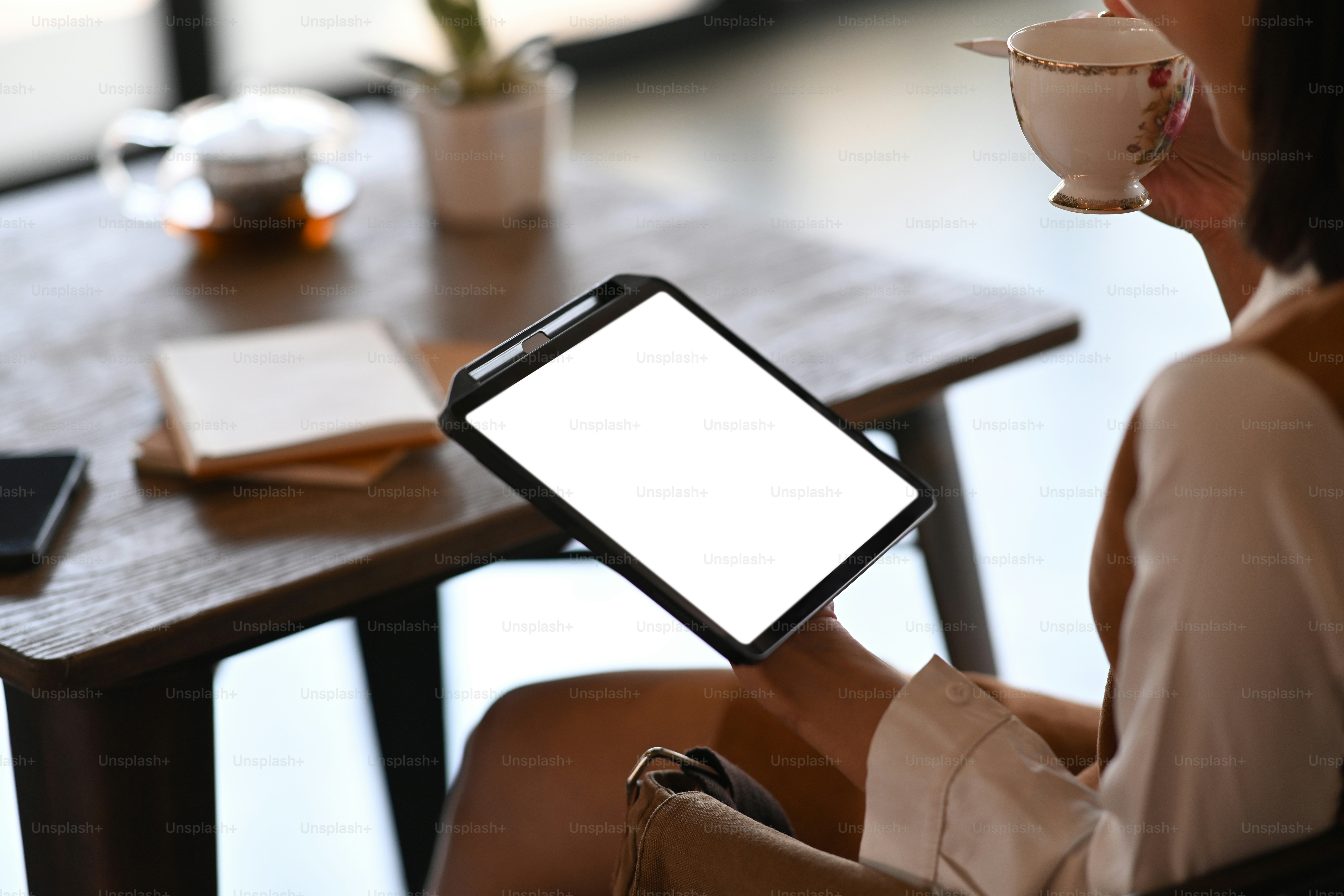 Plan recadré d’une jeune employée de bureau buvant du café et utilisant une tablette numérique pendant une pause au bureau.