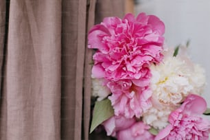 Bouquet di peonie all'elegante vestito di lino in luce soleggiata, primo piano. Vita lenta. Giovane femmina in abito rustico boho che tiene peonie rosa e bianche. Momento estetico
