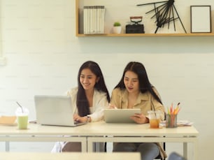 Portraits of two female students using tablet and laptop while doing homework together in cafe