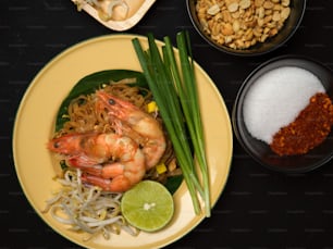 タイの伝統的なプレート、パッタイ、タイ料理、上面図にライム、もやし、チャイブを添えたエビで焼いたタイの麺をかき混ぜる