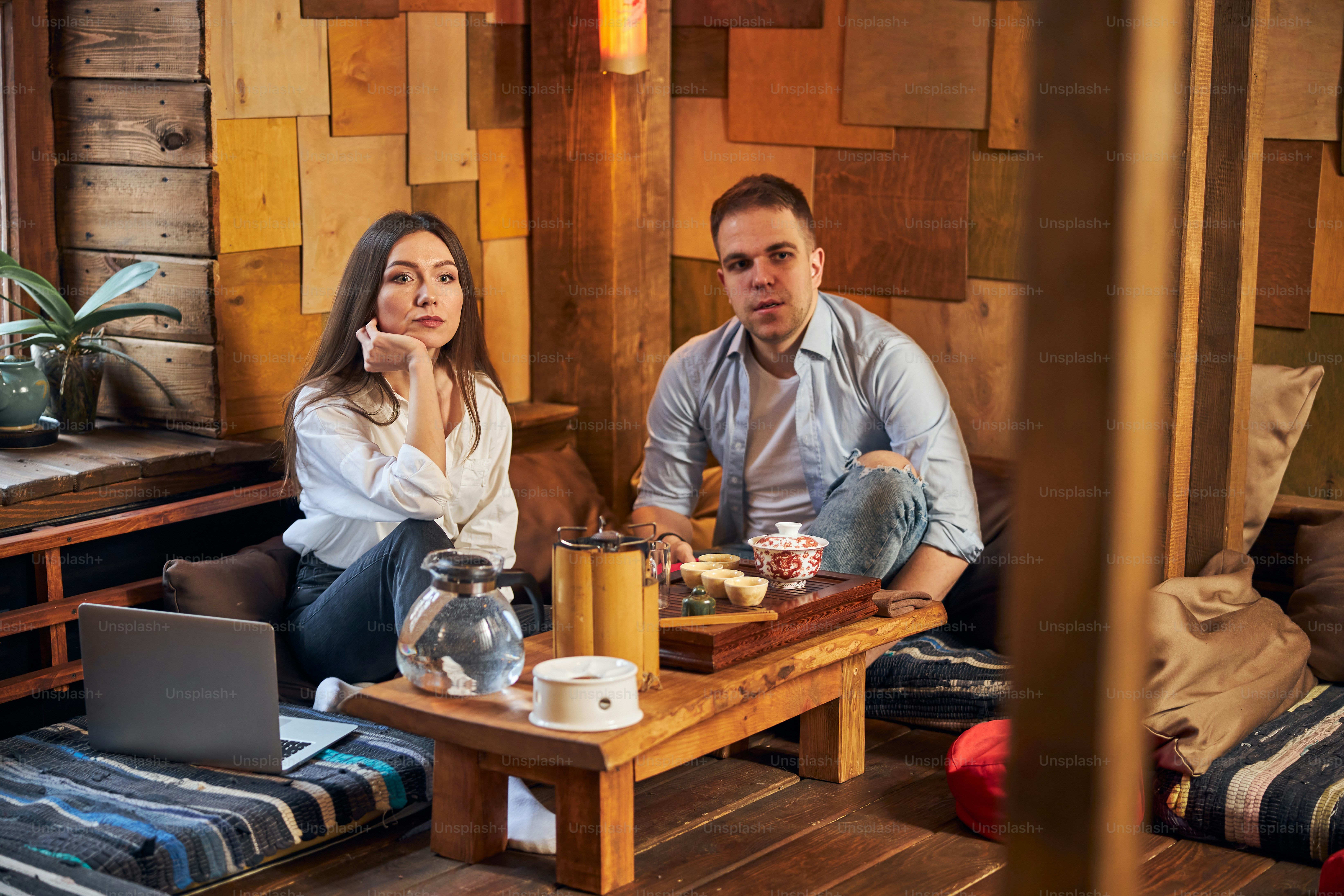 Charming woman sitting at the table near laptop and looking away with serious expression while having meeting with male friend