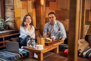 Charming woman sitting at the table near laptop and looking away with serious expression while having meeting with male friend