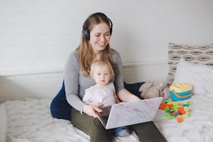 Young Caucasian mother with toddler baby working on laptop from home. Workplace of freelance woman student with kid. Online learning education or work job during self isolation, quarantine.