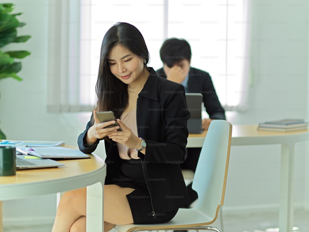 Portrait of businesswoman using smartphone to relax while sitting at workspace in office room