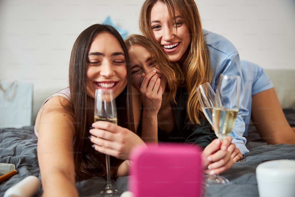 웃고 있는 검은 머리의 아가씨가 핸드폰으로 자신과 그녀의 씩씩한 여자 친구들의 사진을 찍고 있다