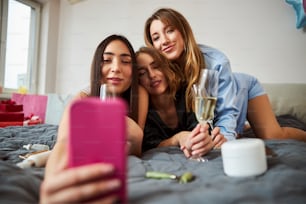 Front view of a dark-haired woman photographing herself and her blonde friends with the smartphone