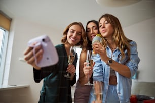 Schöne Frauen mit Gläsern Sekt posieren für die Sofortbildkamera auf einer Karaoke-Party
