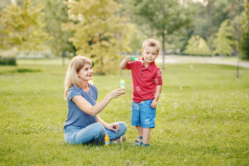 젊은 백인 어머니와 소년 유아 아들은 공원에서 비누 방울을 불고 있습니다. 엄마와 아이는 여름날 야외에서 함께 놀고 있습니다. 행복 한 정통 가족 어린 시절 생활 방식.