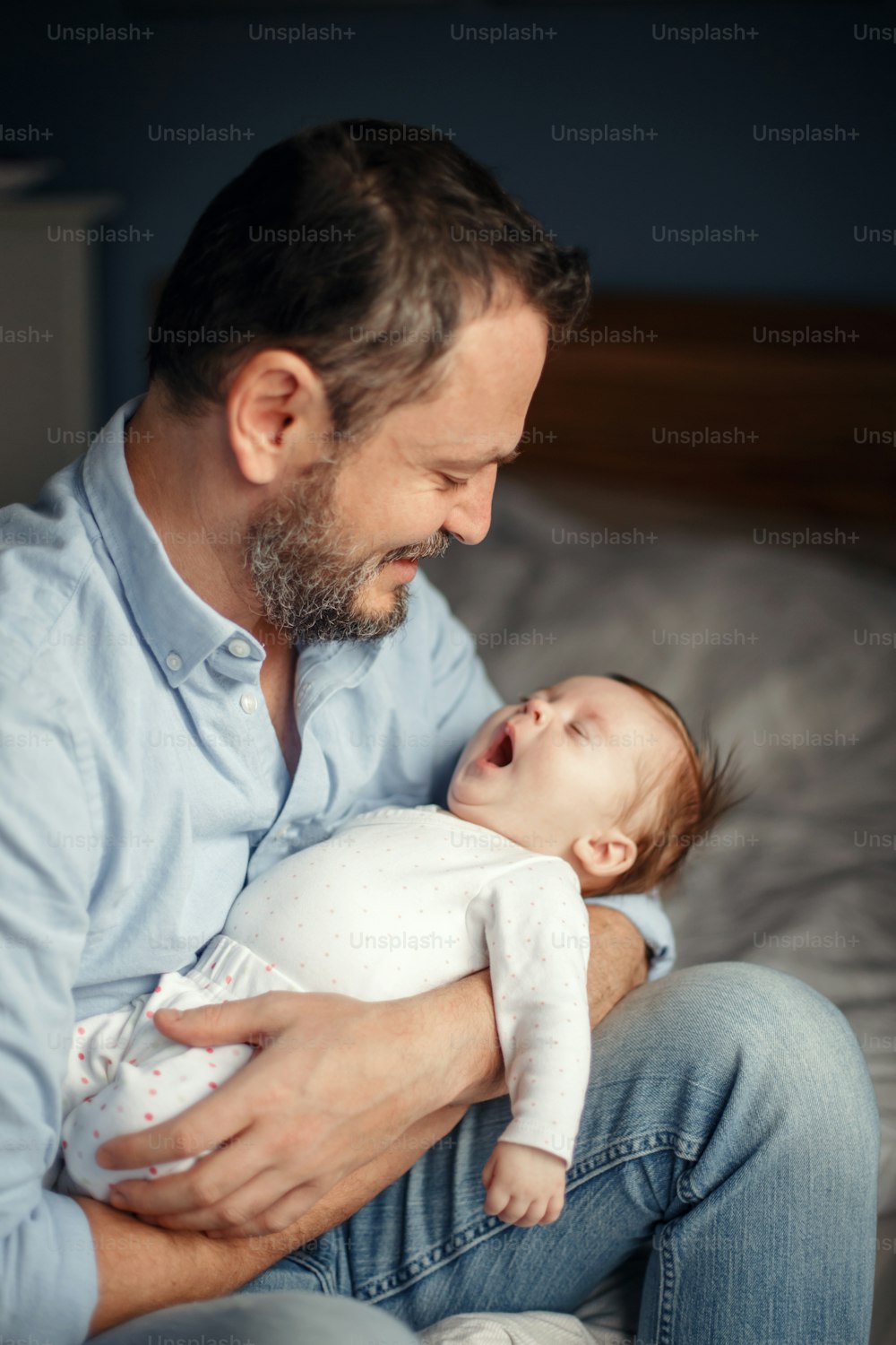 Middle age Caucasian father with sleeping yawning newborn baby girl. Parent holding rocking child daughter son in hands. Authentic lifestyle parenting fatherhood moment. Family home life.