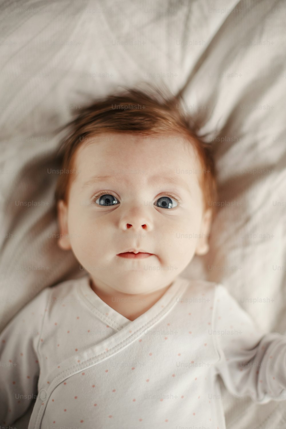 Retrato de primer plano de un lindo bebé recién nacido caucásico. Adorable y divertido bebé infantil con ojos azules grises y cabello rojo acostado en la cama mirando a la cámara. Auténtica infancia y estilo de vida momento sincero.