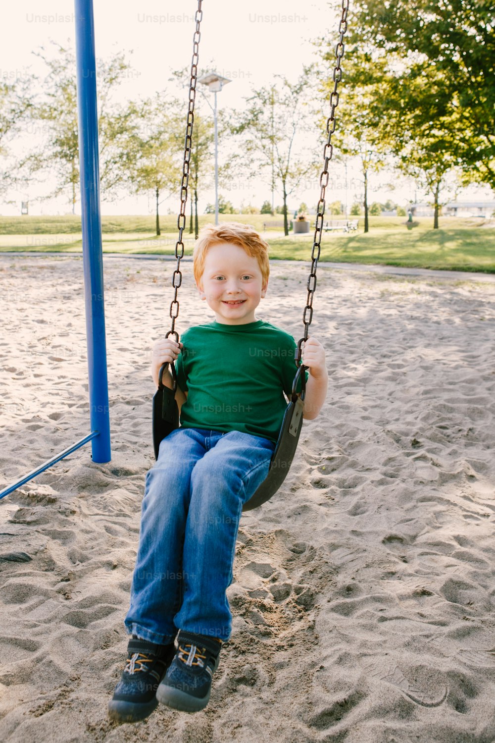 Happy smiling little preschool boy swinging on swing-set playground outside on summer day. Happy childhood lifestyle concept. Seasonal outdoor activity for kids.