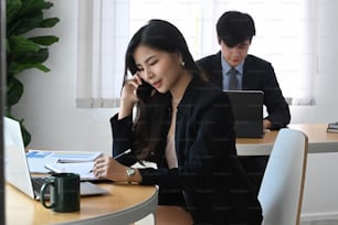 Attractive businesswoman talking on mobile phone and analyzing business data at modern office.