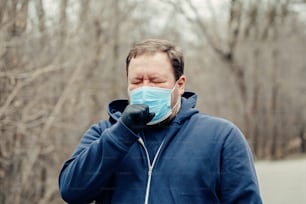 Giovane uomo di mezza età caucasico in maschera sanitaria starnutisce tosse all'aperto. Persona che protegge dalla pericolosa diffusione del virus. Quarantena della malattia da Coronavirus COVID-19.