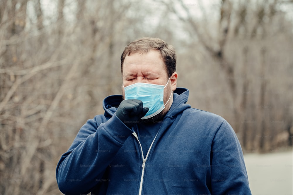 Caucasian young middle age man in sanitary face mask sneezing coughing outdoor. Person protecting from dangerous spread of virus. Coronavirus COVID-19 disease quarantine.