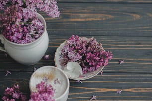 Café avec des pétales de lilas, des branches de lilas en fleurs dans une tasse vintage sur fond en bois foncé. Café frais et aromatique dans une tasse élégante et des fleurs printanières sur du bois rustique. Rituels matinaux