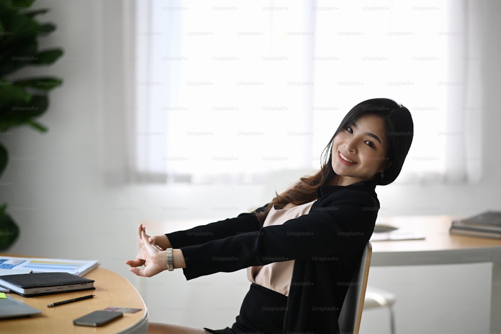 Cheerful businesswoman relaxing and stretching her body at her workplace.