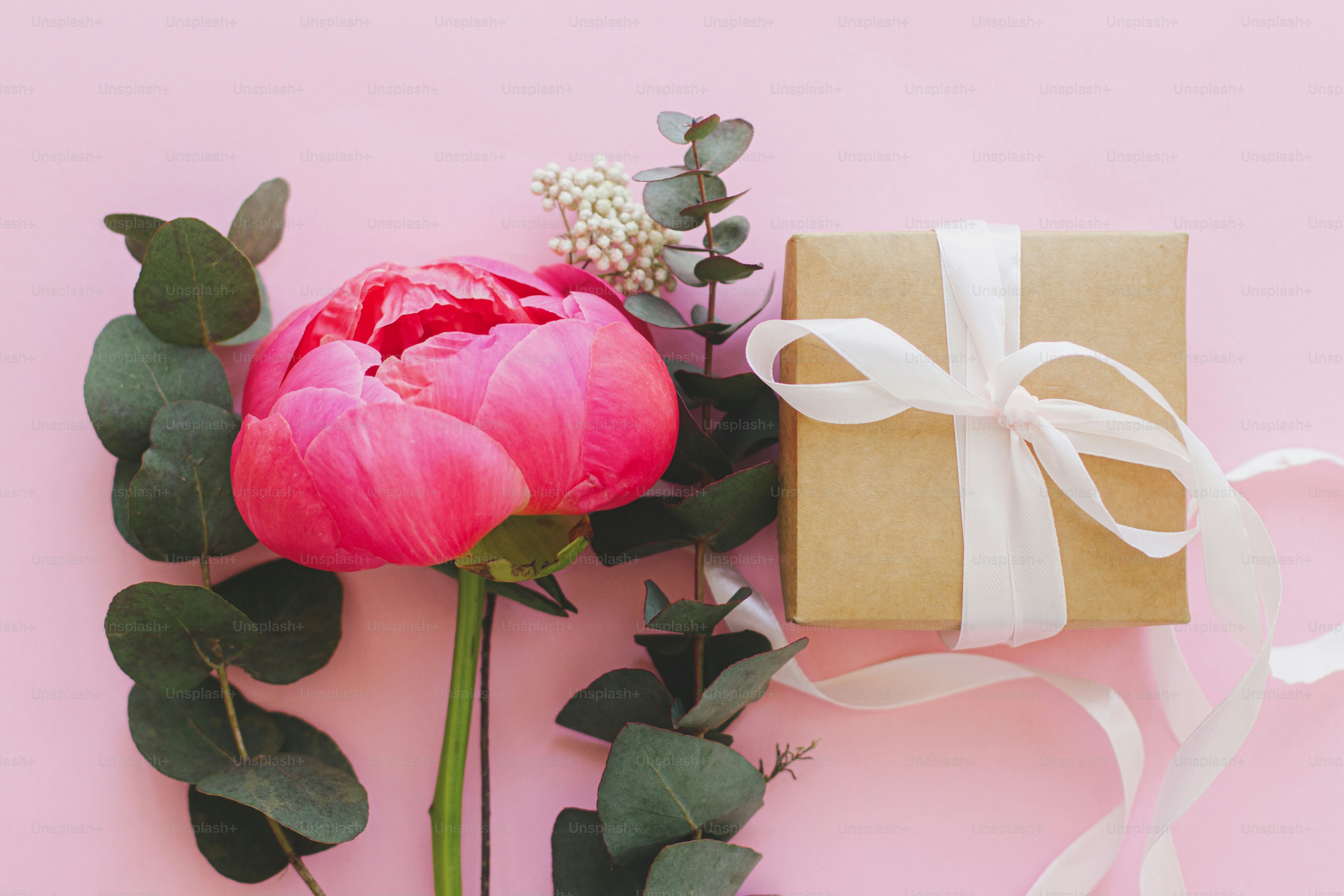 Modern minimal bouquet and simple gift box with ribbon on bright pink background flat lay. Stylish colorful greeting card with peony and eucalyptus. Happy womens day or mothers day.