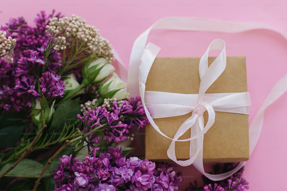 Semplice confezione regalo con nastro e bellissimo bouquet di lilla e rose piatto su sfondo rosa brillante. Buona festa della mamma o festa della donna, elegante biglietto d'auguri colorato.