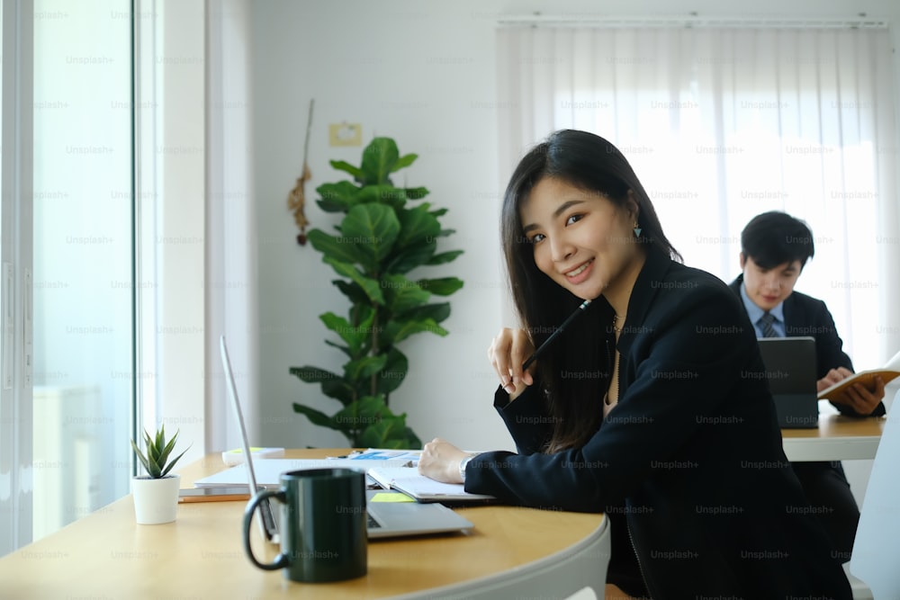 Attractive businesswoman sitting at office desk and smiling to camera.