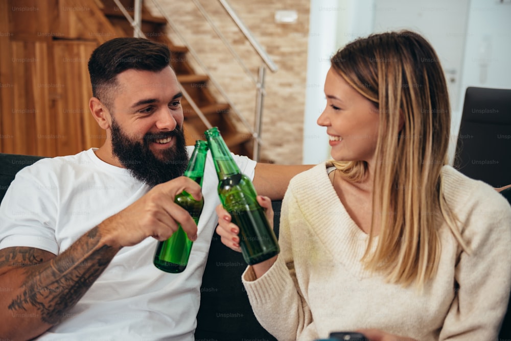 Plan d’un jeune couple buvant une bière tout en regardant le match à la maison