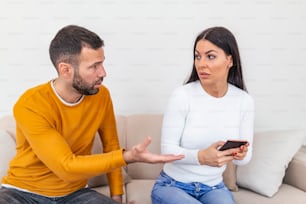 Boyfriend asking for an explanation to his cheater sad girlfriend sitting on a couch in the living room in a house interior