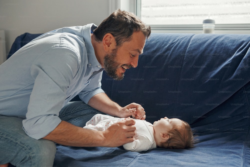 Proud Caucasian father talking to newborn baby girl. Smiling happy parent man with daughter son. Authentic lifestyle happy parenting fatherhood moment. Single dad family home life.