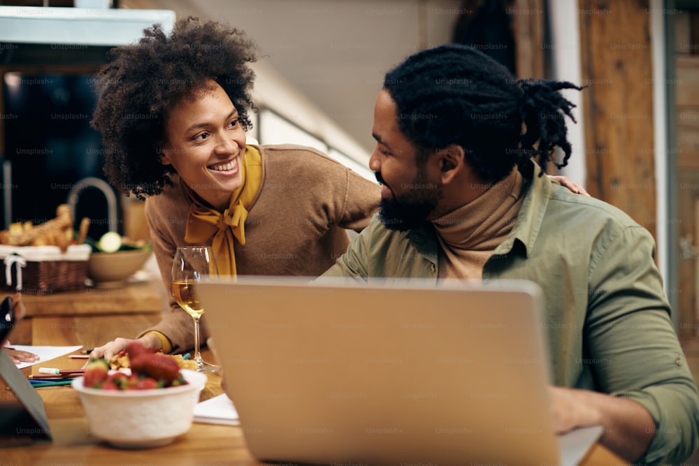 幸せなアフリカ系アメリカ人のカップルは、自宅でラップトップを使用しながら通信しています。焦点は人間にあります。