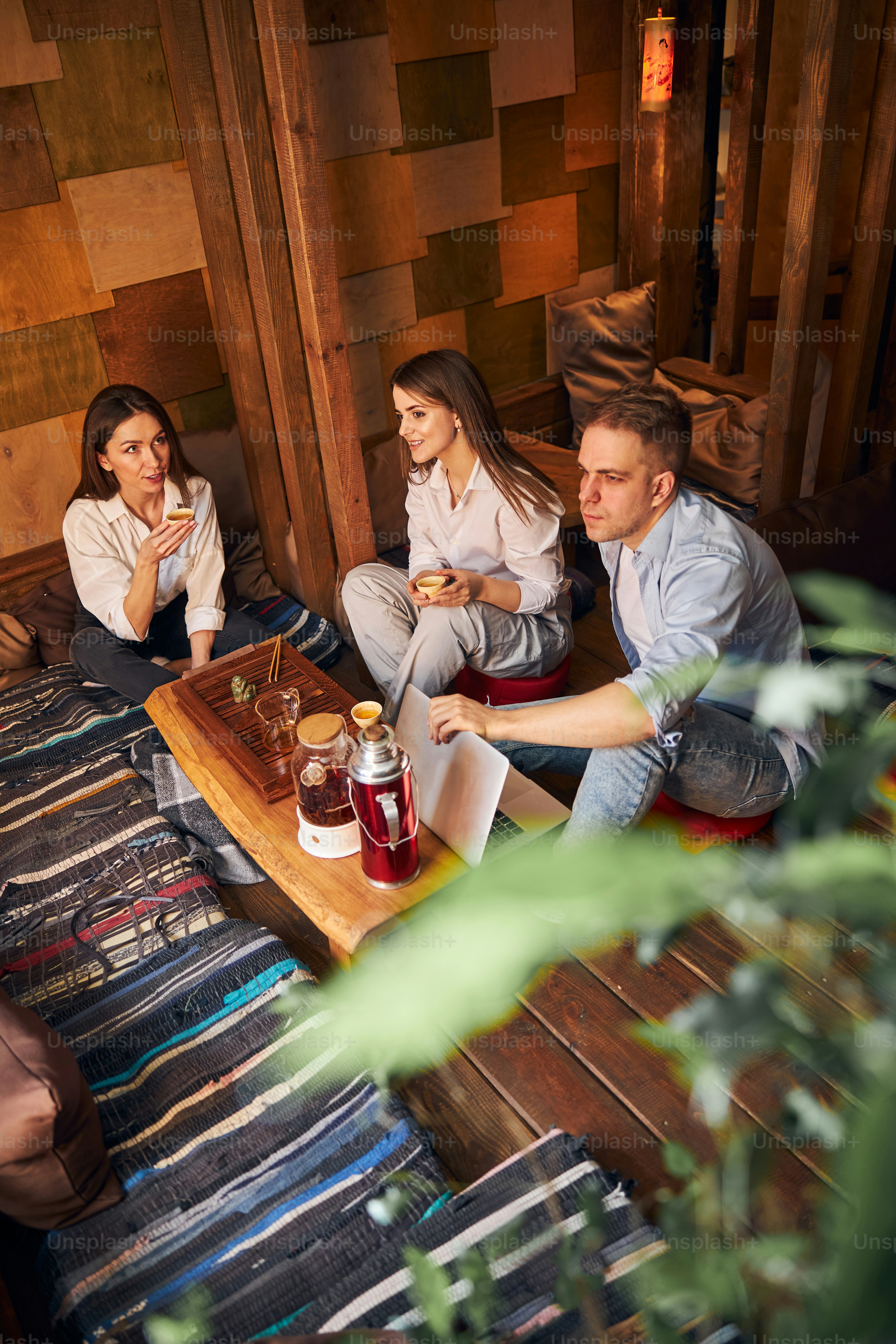 Charming young women and man enjoying tea ceremony and communicating while sitting at the table in tea house