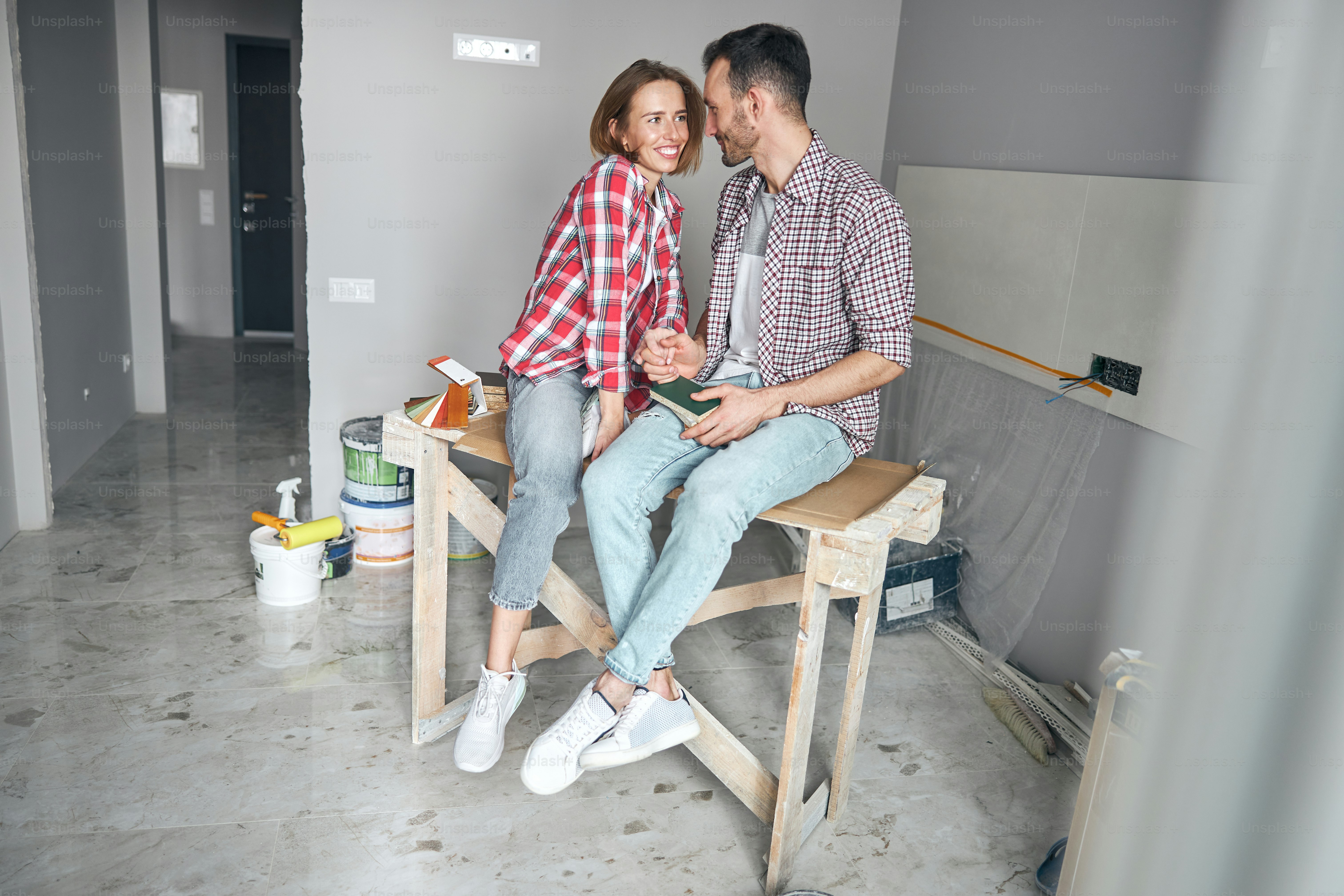 High-spirited lovely blonde female sitting on a wooden table next to a dark-haired male worker