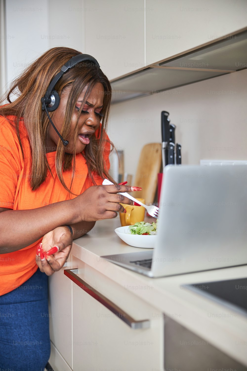 Young African - American woman looking shocked while poking in her salad bowl near open laptop