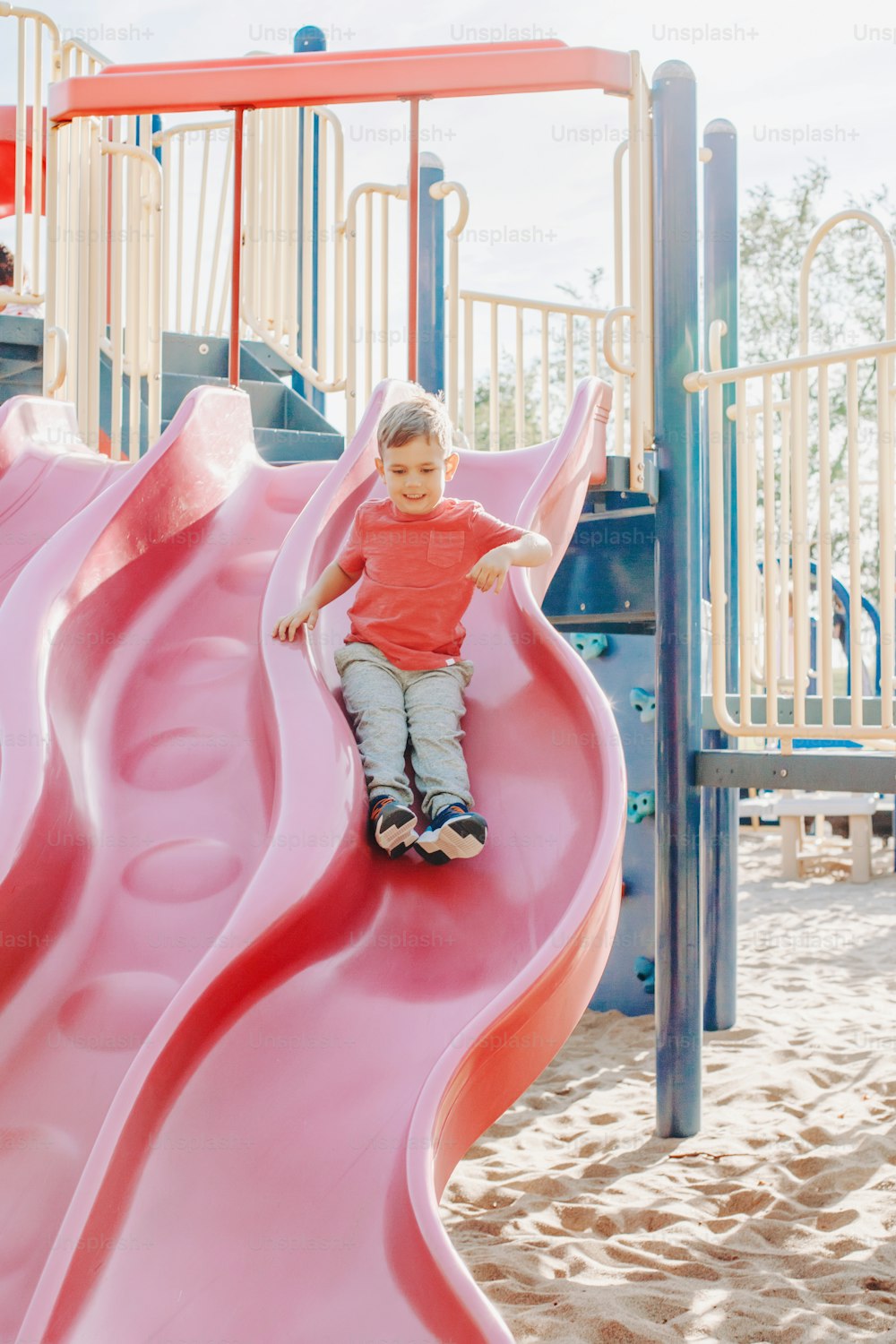 Active happy smiling Caucasian boy sliding on playground. Kid on schoolyard outdoors on summer sunny day. Child having fun outside on play ground. Seasonal sport kids activity.