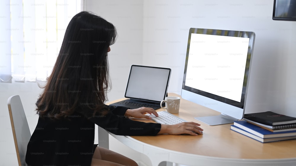 Side view of of businesswoman working with multiple devices at office desk.