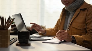 黄色いジャケットを着た若い男性が自宅でラップトップコンピュータを使ってオンラインで作業しているショットをトリミングしました。