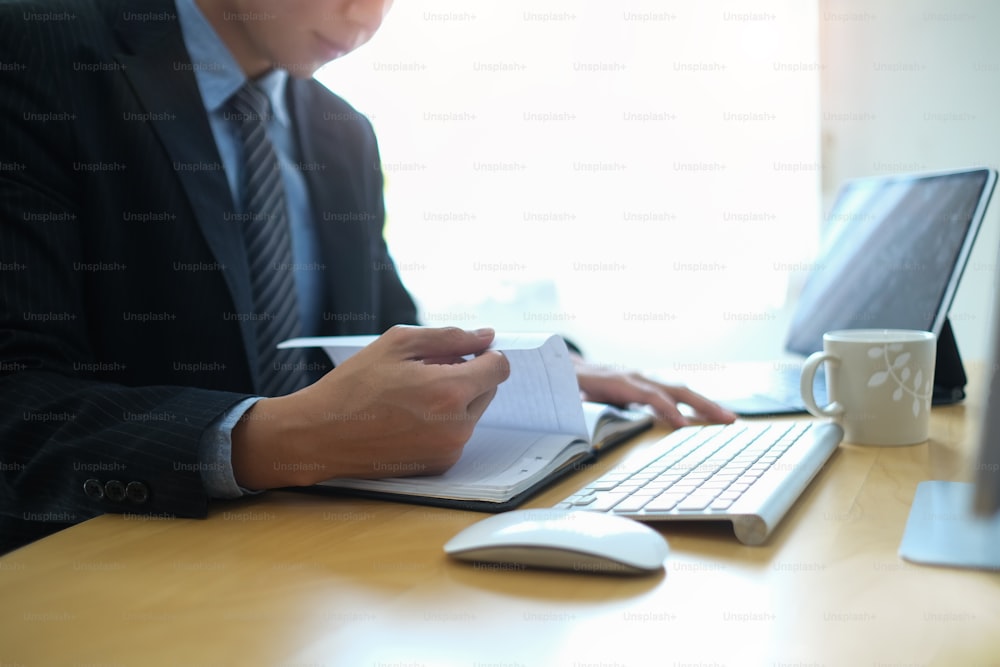 Cropped shot of businessman working with computer tablet and reading information on notebook at office.