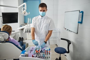 Joven médico masculino sacando instrumentos dentales de una bolsa autosellante en el consultorio de un dentista