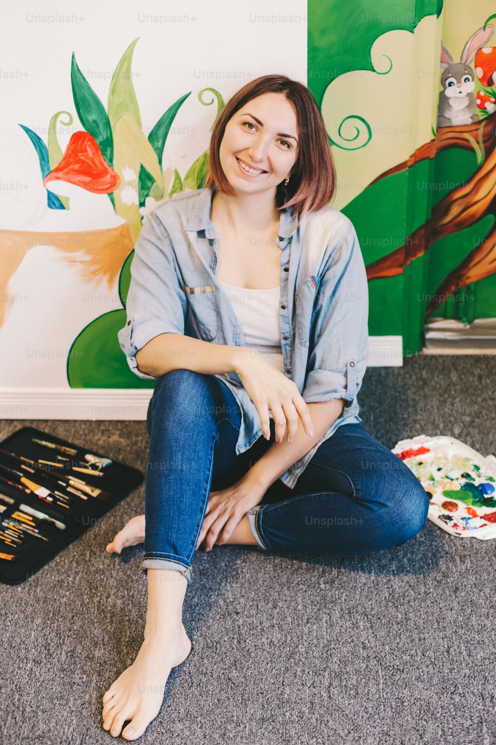 백인 여성 예술가는 아크릴 물감으로 아파트 또는 스튜디오 학교의 실내 벽에 벽화를 손으로 그린 후 휴식을 취합니다. 창의적인 취미와 프리랜서 예술 작업 부업 개념.