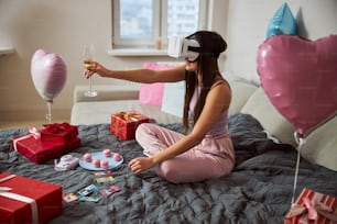 Vista lateral de una dama de cabello oscuro con gafas de realidad virtual que sostiene una copa de champán en la mano