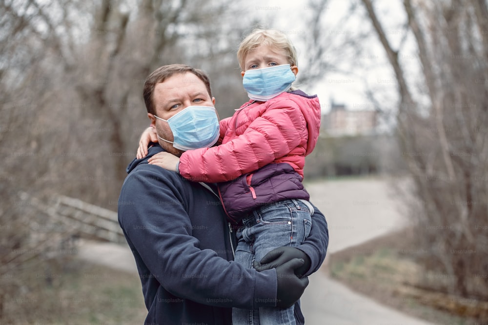 Kaukasischer Vater mit Kind Mädchen trägt hygienische Gesichtsmasken im Freien. Familienvater und Tochter schützen sich vor einer gefährlichen Ausbreitung des Virus. Coronavirus COVID-19 Quarantäne.