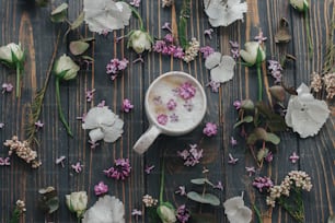 Caffè con petali lilla piatti su sfondo di legno scuro con spazio per il testo. Caffè fresco e aromatico in elegante tazza e fiori e petali primaverili su legno rustico. Rituali mattutini estetici