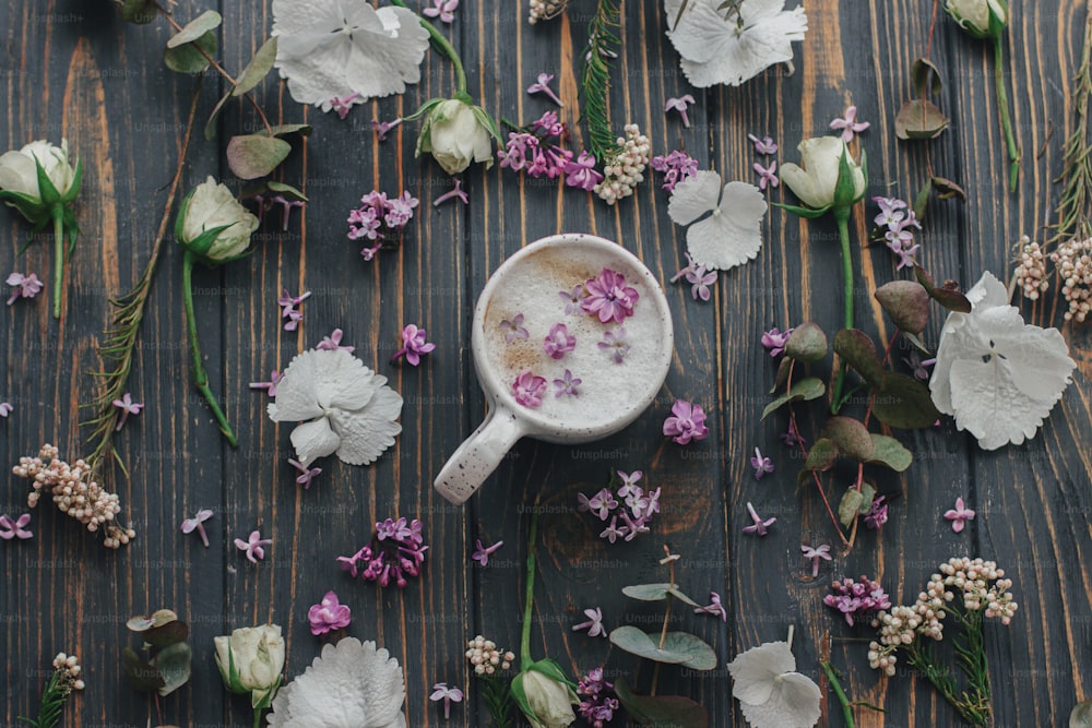Coffee with lilac petals flat lay on dark wooden background with space for text. Fresh aromatic coffee in stylish cup and spring flowers and petals on rustic wood. Morning rituals aesthetic