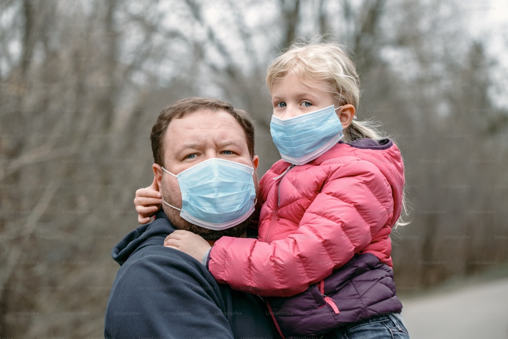Kaukasischer Vater mit Kind Mädchen trägt hygienische Gesichtsmasken im Freien. Familienvater und Tochter schützen sich vor einer gefährlichen Ausbreitung des Virus. Coronavirus COVID-19 Quarantäne.
